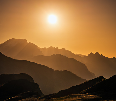 Sun glow in evening hazy sky and mountain silhouettes view.  Peaceful view from Giau Pass. Climate, environment and travel concept scene.