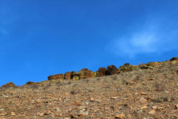 Lichen Covered Rock on Top of Cliff against Blue Sky