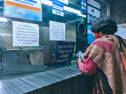 Kolkata, 02/05/2021: A woman (wearing face mask) standing near ticket counter inside a Kolkata Metro Railway station. There are various informative notice stuck on wall, mainly announcing that due to covid-19 pandemic, no 'entry token' will be issued, only 'smart card' holders can travel metro.