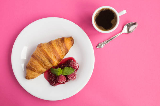 istock Continental breakfast with croissant, coffee  and raspberry jam on the pink background 1306856043