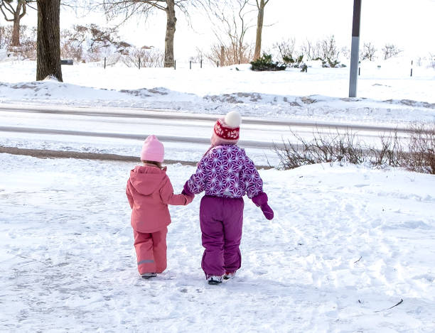 deux petites filles de 3 et 5 ans, se tiennent la main et vont à la route de la ville. danger sur la route. prendre soin des enfants. - child caucasian little girls 3 4 years photos et images de collection