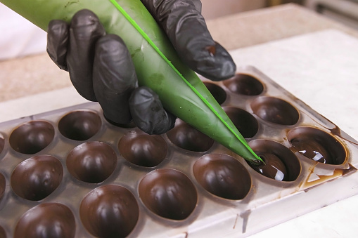 Baker's hands pouring liquid chocolate filling praline in form from pastry bag