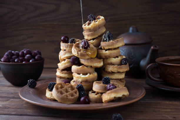 istock a stack of waffles decorated with berries. Honey is pouring from above. waffles lie on a clay plate on a wooden table 1306860766