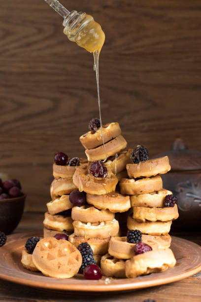 istock a stack of waffles decorated with berries. Honey is pouring from above. waffles lie on a clay plate on a wooden table 1306860817
