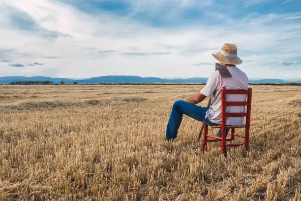 Photo of Farmer with straw hat and hoe sitting on a red chair in the middle of the field