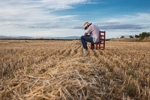 Farmer with straw hat and hoe sitting on a red chair in the middle of the field. Agriculture concept.