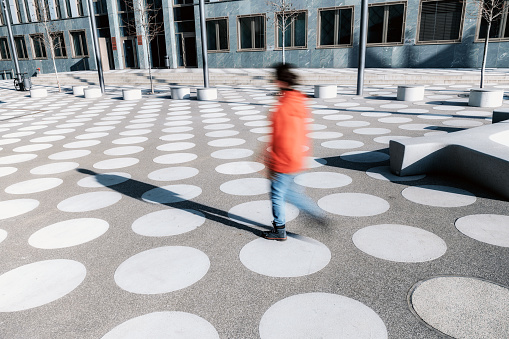 motion blur of girl in red jacket going on asphalted town square with white dots in berlin
