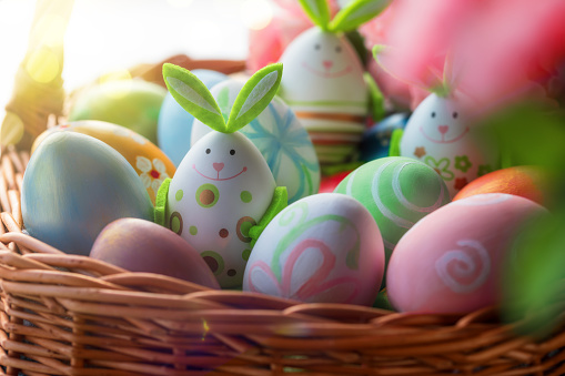 Easter decoration with crafted bunny and Easter eggs in the wicker basket. Spring Easter composition with defocused pink flowers on foreground.
