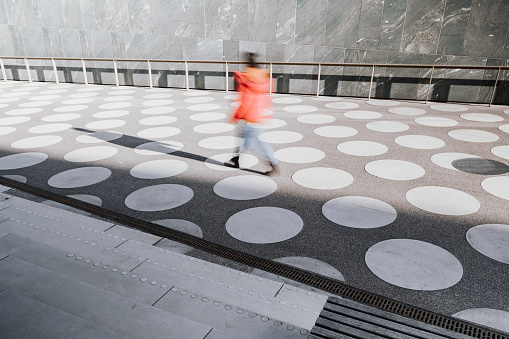 motion blur of girl in red jacket going on asphalted town square with white dots in berlin