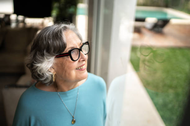 istock Senior woman looking through window at home 1306876910