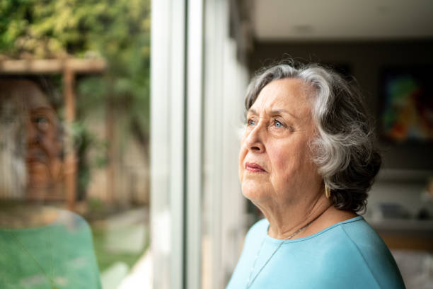 istock Serious senior woman looking through window at home 1306876922