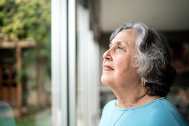 istock Senior woman looking through window at home 1306876989