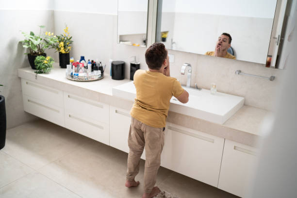 Young man with dwarfism looking in the mirror in the bathroom Young man with dwarfism looking in the mirror in the bathroom short stature stock pictures, royalty-free photos & images