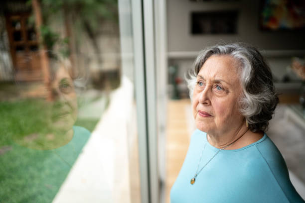 istock Serious senior woman looking through window at home 1306877017