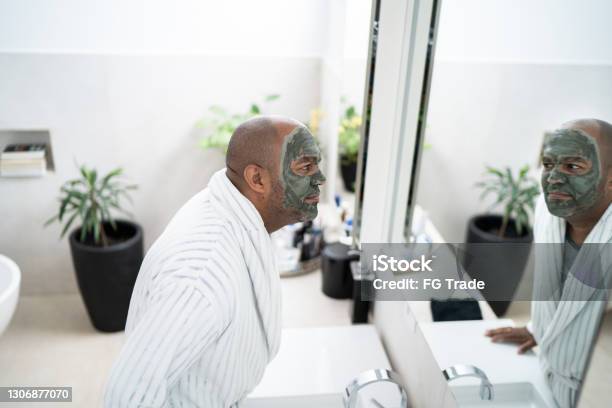 Mature man with facial mask looking in the mirror - clay mud