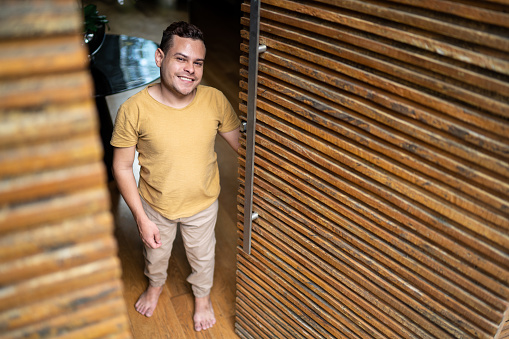 Portrait of a happy young man with dwarfism opening the door