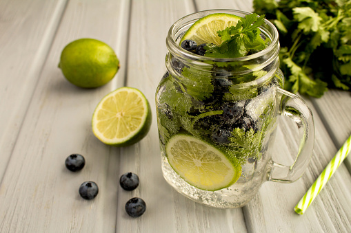 Infused or detox water with blueberries, cilantro and lime  on the  gray wooden  background. Close-up.