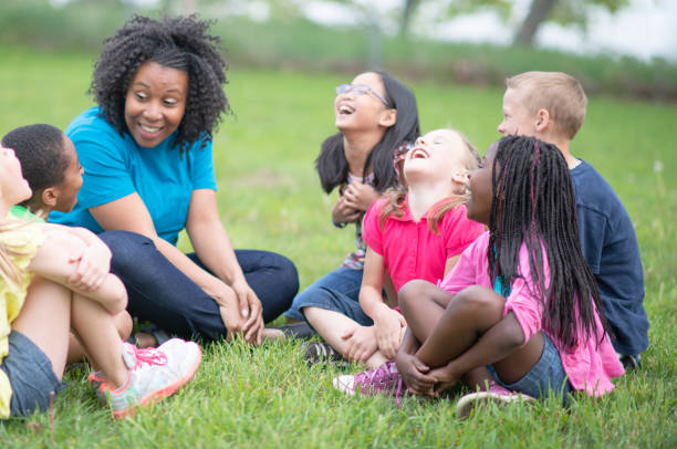 Camp Counselor and Children at Summer Camp A female camp counselor is sitting on the grass with her group of children at a public park. She is telling them a story. The children are happy and smiling. summer camp photos stock pictures, royalty-free photos & images