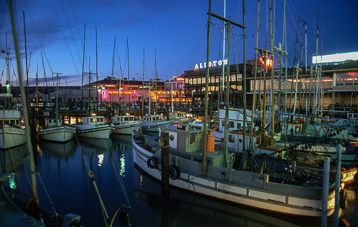 Fisherman's Wharf, San Francisco, California, at night with docked fishing boats in the foreground and restaurants with neon signs. Scanned film, June 1974.