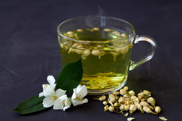 cierra el té de jasmine. taza de té de hierbas calientes con flores frescas de jazmín en una mesa negra. estilo de vida saludable. vaso taza de té verde con hojas secas sobre un fondo negro. bebidas calientes. - jasmine tea jasmine herbal tea drink fotografías e imágenes de stock