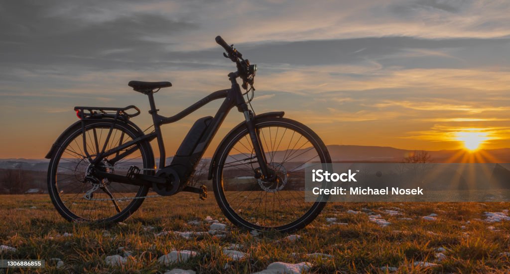 Black and gray electric bicycle in sunrise morning time on frosty field Black and gray electric bicycle in sunrise morning time on frosty field with yellow sun Electric Bicycle Stock Photo