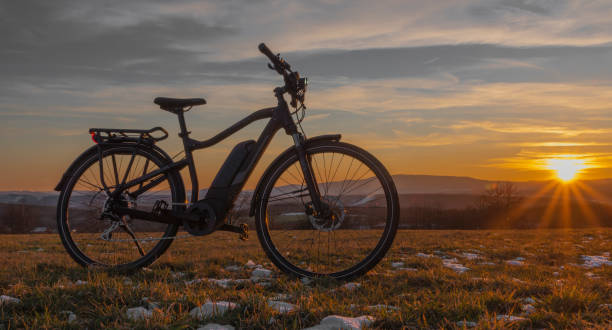 Black and gray electric bicycle in sunrise morning time on frosty field Black and gray electric bicycle in sunrise morning time on frosty field with yellow sun electric bicycle stock pictures, royalty-free photos & images