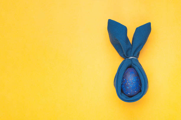 istock Easter decoration with rabbits blue napkin and egg on a yellow background. Easter concept. Copy space, top view, 1306888441
