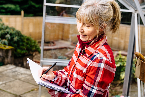 Woman in her greenhouse planning the summer ahead with pen and note pad.