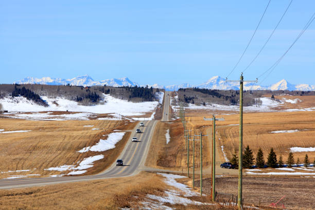 Heading Back From The Winter Canadian Rockies On A Rural Alberta Highway Alberta  rural highway between Calgary and Cochrane looking West.  Early March.  Snow covered Rocky Mountains in Distance. cochrane alberta stock pictures, royalty-free photos & images