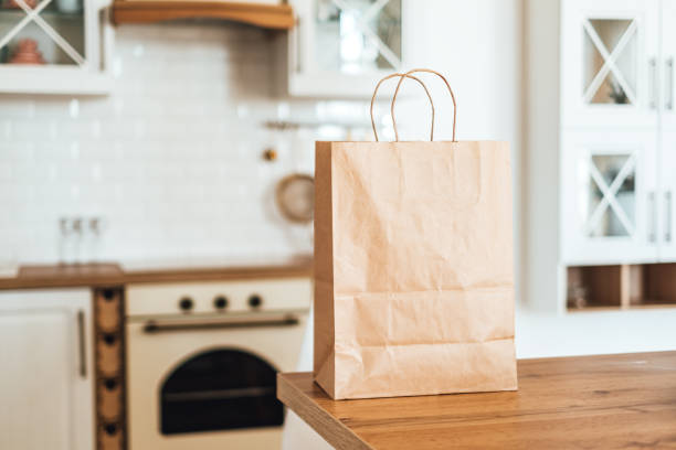 saco de papel de compras ecológicas sobre a mesa na cozinha moderna. entrega de alimentos ou conceito de compras de mercado. - green consumerism bag paper bag - fotografias e filmes do acervo
