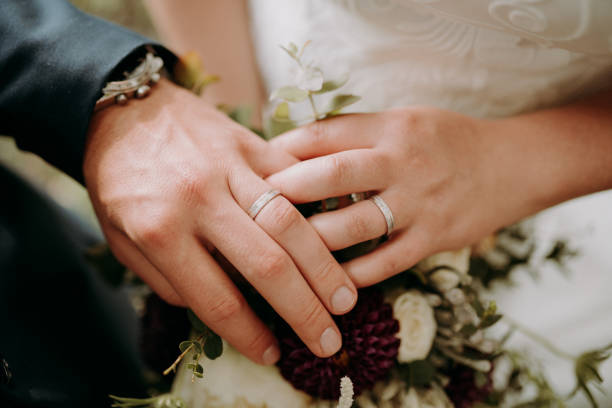 istock gold wedding rings on two hands with flower 1306896883