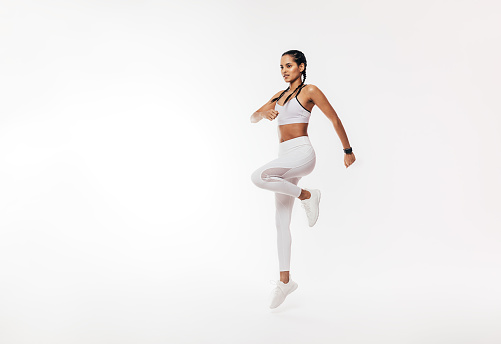 Young fit woman exercising over white background. Female in white sportswear jumping