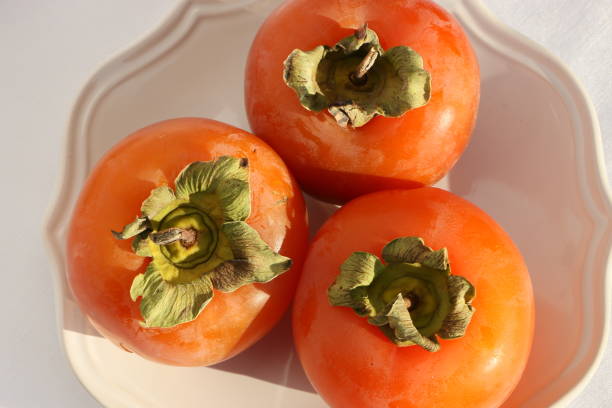 istock Fresh ripe persimmons on a white plate with a classic design on a white tablecloth, Paradise Palms 1306897832