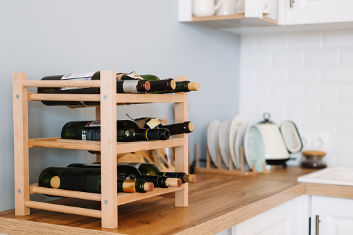 Wooden wine shelves with bottles on the table in modern kitchen.