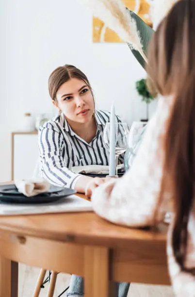 Young woman supports her best friend, consolation holding her hand while sitting at the table in the kitchen at home.