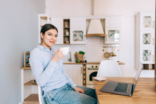 istock Young caucasian woman drink coffee and using laptop computer while sitting on chair in modern kitchen. 1306900321