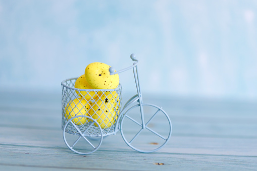 White toy bicycle with yellow Easter eggs. Easter greeting card with abstract scene with eggs in yellow colors. Delivery on Easter.