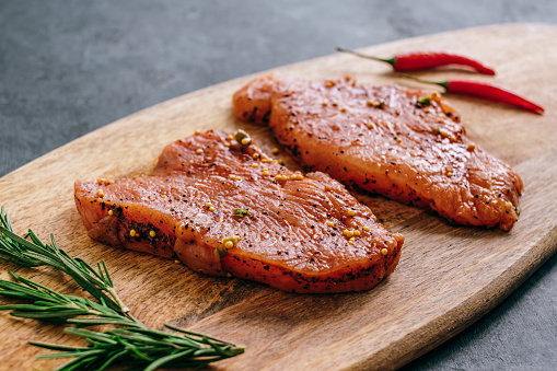 Marinated turkey steak on a wooden board with rosemary and chili pepper..