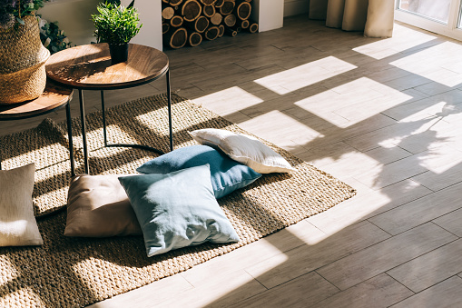 Interior of bright living room in scandinavian style with coffee table and pillows on the floor, big shadow from window on the floor.