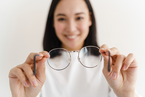Positive, smiling girl holding glasses. Girl on a developed background. Asian.