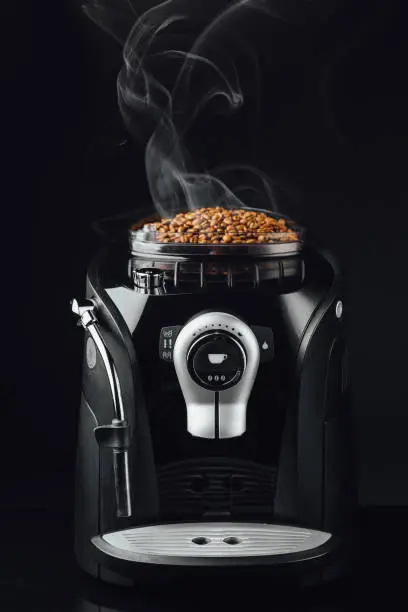 fresh roasted coffee beans with smoke in coffeemaker bean container, close-up view