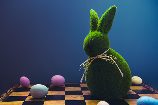 Creative and trendy Easter concept. Easter chess play with colored eggs and Easter green bunny rabbit on the dark blue background. Selective focus, copy space