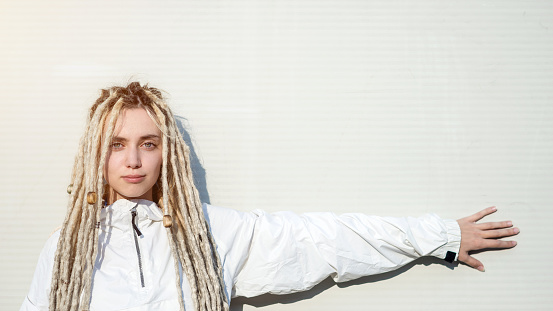 Young modern fashionable woman with blond dreadlocks hair pointing with her hand on the wall