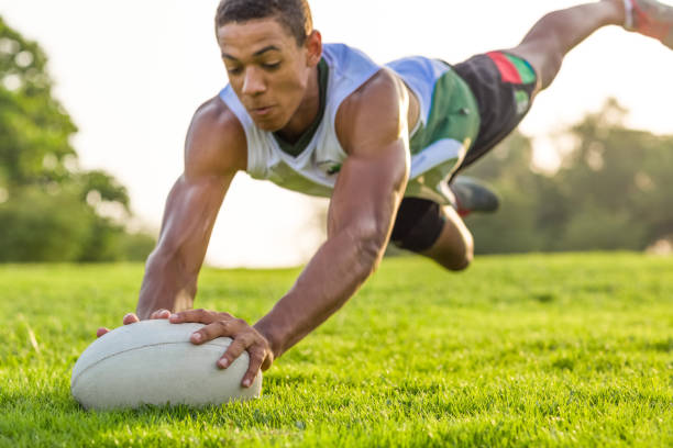 Athletic athlete in action jumping in the air for the rugby ball on the grass. Outdoor sport. Muscular rugby player in the air diving for the ball on the sport field. athleticism photos stock pictures, royalty-free photos & images
