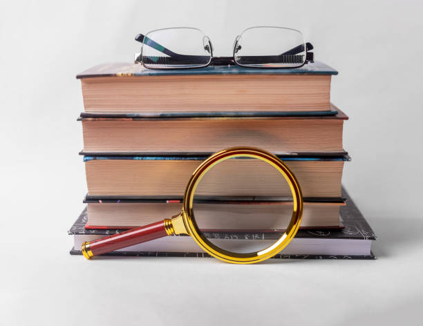 istock Stack of books with magnifier and glasses on white background 1306926195