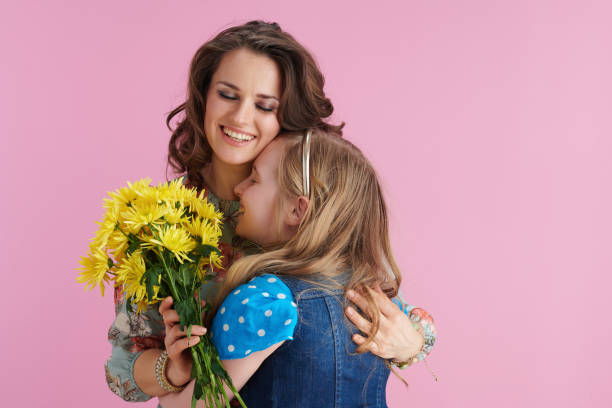 smiling elegant mother and child embracing on pink smiling elegant mother and child with long wavy hair with yellow chrysanthemums flowers embracing against pink background. april 10 stock pictures, royalty-free photos & images