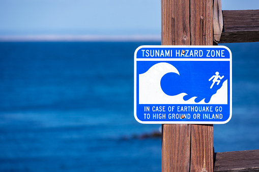 Tsunami Hazard Zone warning sign on the Pacific Ocean coast warn the public about possible danger after an earthquake. Blue ocean in background