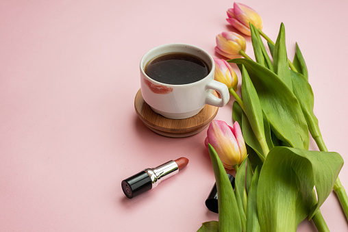 Cup of coffee, cosmetics and bouquet of tulips on pink background, top view. Women's day or Mother's day concept. Creative flat lay.