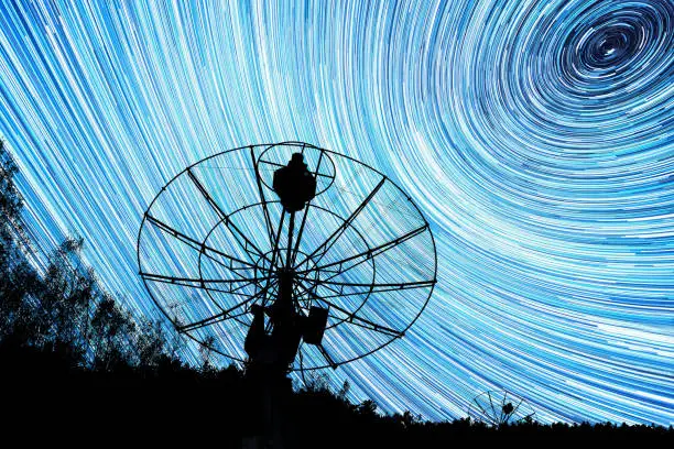 radiotelescopes silhouettes under long star trails background