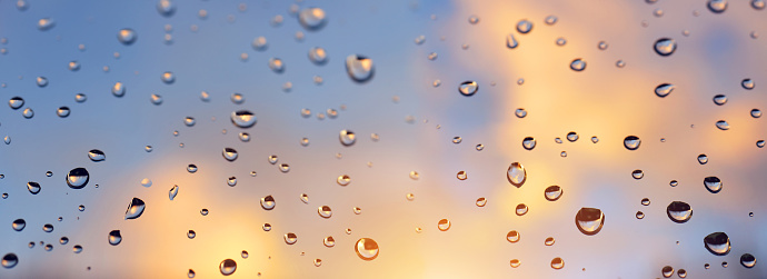 Water drops on a window glass after the rain at sunset. Panoramic nature background.